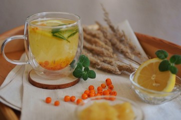 A cup of sea buckthorn tea with mint, lemon and honey with rustic background