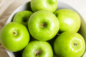Green apples in a bowl on a light fabric background. Harvest apples, summer season, fresh fruits. Top view.