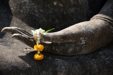 Yellow flower garland in hand, Buddha statue in Sukhothai Historical Park in Sukhothai Province Thailand.
