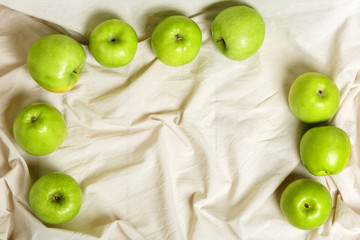 Green apples on a light fabric background. Harvest apples, summer season, fresh fruits. Top view, flat lay. copy space.