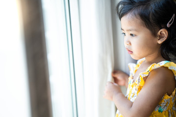 Cute little girl standing at window lookin outside during Covid 19 Quarantine.