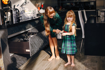 Fototapeta premium Beautiful mother with little daughter. Family works in the kitchen. Two ladies in a green dress