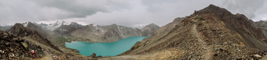 Kyrgyzstan. Karakol. Alakel. A beautiful alpine lake of turquoise color among high snow-capped mountains. Panoramic photo