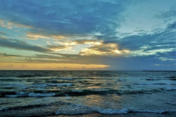 Sunset over the Indian Ocean. Aquamarine waves slowly rush ashore. The sky and clouds are painted in shades of blue and gold.