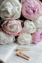A beautiful bouquet of white and pink peonies lie on an open book. On the book next to the bouquet are beautiful hair clips. Vintage hair clips. Present.