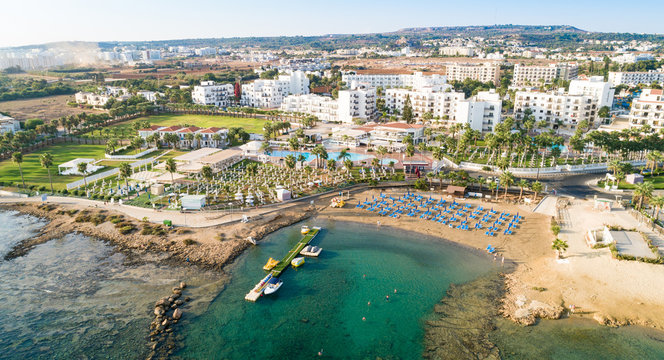 Aerial bird's eye view Pernera beach Protaras, Paralimni, Famagusta, Cyprus. The tourist attraction golden sand bay with sunbeds, water sports, hotels, restaurants, people swimming in sea from above.