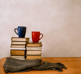 stacks of books, striped scarf, two blue and red cups, white background and place for text