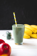 The concept of food and drink, diet and nutrition. Healthy green vegan smoothie with banana, spirulina and ripe apple for summer detoxification