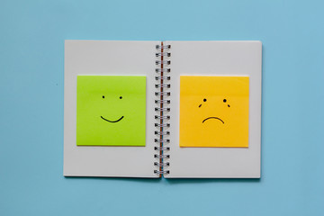 Smile face with Cry face on sticky paper note on notebook on blue background.