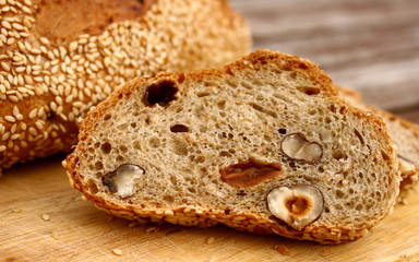 closeup slice of rye bread with hazelnuts and raisins on wooden board, whole bread next to it