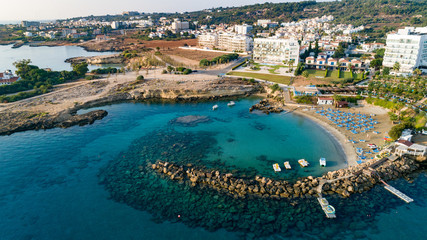 Fototapeta na wymiar Aerial bird's eye view of Green bay in Protaras, Paralimni, Famagusta, Cyprus. Famous tourist attraction diving location rocky beach with boats, sunbeds, sea restaurants, water sports from above.