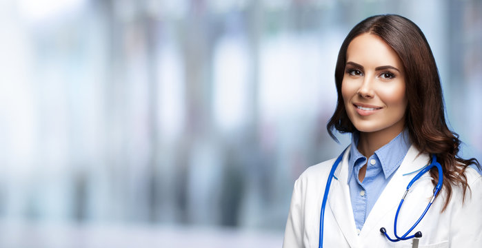 Portrait picture of happy smiling female doctor in white uniform coat and stethoscope, standing blurred office background. Healthcare, medical, medicine specialist - concept. Copy space.