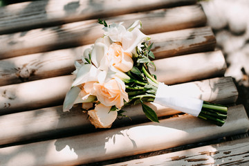 A wedding bouquet of roses and calla lilies lies on a wooden background.