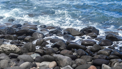 Breakwater stones on a jetty on a balinese black beach. Sea view and background.
