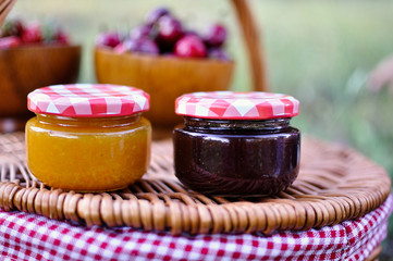 Two jars of homemade jam on wicker basket in the field.