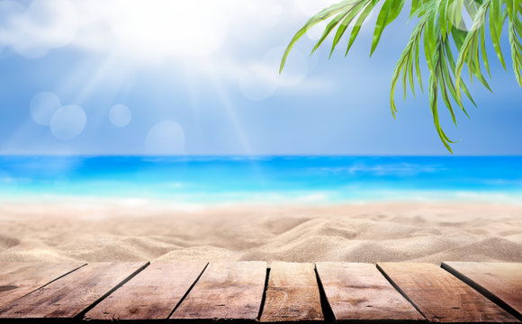 A Wooden Table Product Display With A Summer Vacation, Holiday Background Of A Tropical Beach, Blue Sea, White Clouds, Sun Flare And Green Palm Tree Leaves.