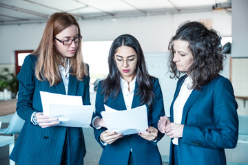 Group of focused women reading paper documents. Front view of professional business team with instructions. Business concept