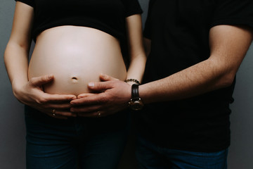 Hands of a man and a woman hug a pregnant belly. Young parents waiting for the baby