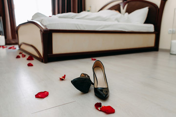 Scattered women's shoes in a hotel room on the background of the bed. Romantic atmosphere.