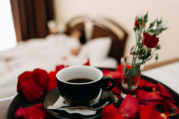 Aromatic coffee in a cup stands on a tray lined with rose petals. Breakfast in the room