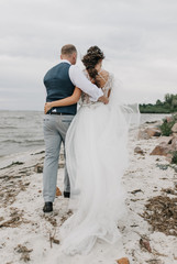 rear view of bride and groom in boho style hugging in walk along the beach