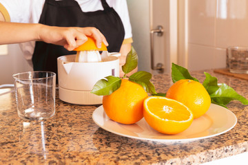 Teen girl holding a citrus juicer with orange and fresh citrus fruit in the kitchen.