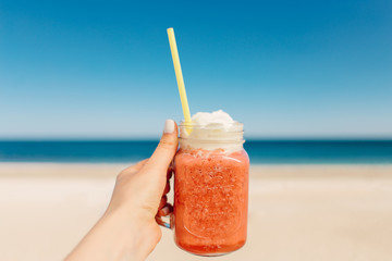 Fruit smoothie in a glass jar in hand on a background of the sea. Summer cocktail