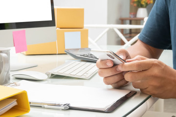 Fototapeta premium close up of work place and hand of business man using smart phone and desktop computer for work from home job, online telecommunication technology device for social media and e-commerce business