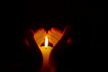 Female hands holding a burning candle in a heart shape on dark background