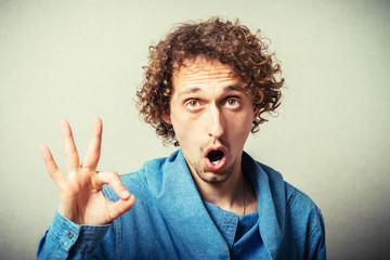 Curly young man makes a gesture okay. On a gray background