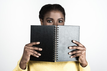 Cute African American student covering face with open notebook. Attractive young lady with notepad looking at camera. Education, tuition concept