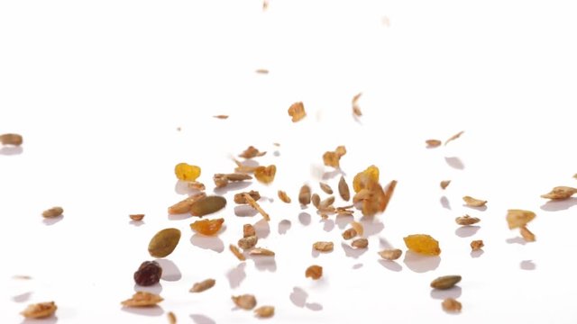 Slow motion speed close up scene of granola dropping on floor on white background, muesli texture, pattern of seed scattered falling and bounce on ground, cereal grain for good health, food industrial