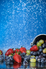 Fruit salad close up in falling metal bucket. Strawberry, grape, blueberry multivitamin cocktail. Healthy lifestyle. Summer diet. Set of fruits under the water drops.