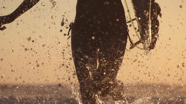 Surfing in the tropics. Young slim woman surfer runs from the ocean with surfboard and lots of splashes