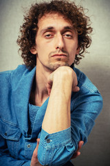 Curly young man serious and unhappy looking at the camera, put his head on his hand. On a gray background