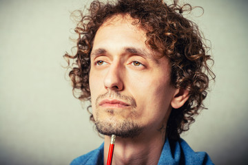 Curly young man is planning something, making notes with a pencil. On a gray background