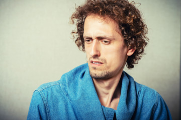 Curly young male resentment and bad mood. On a gray background