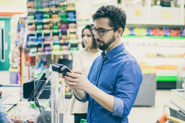 Man using payment terminal in supermarket. Young man buying goods and paying via terminal in grocery store. Shopping concept