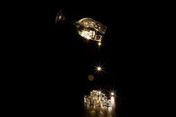 Dropping light sparkle from wine glass on ice cube on dark black background