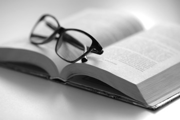 Black and white photo. Reading glasses are located on the spread of the book lying on the sofa. The book is an excellent leisure time during the quarantine period.