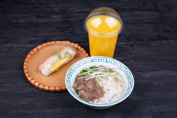 Comprehensive lunch with wax noodle soup, with a roll with shrimp and a glass of juice in a plastic glass