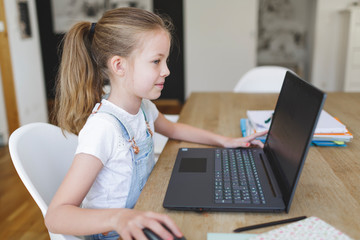 girl sitting in front of her laptop during home schooling during corona crisis and having an e-learning lession