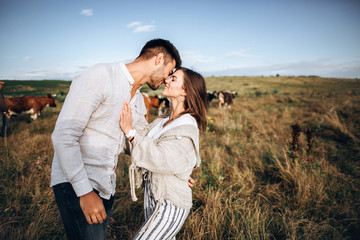 Beautiful loving couple having fun, cuddling, smiling on sky background in field. The guy and the girl hipster kissing
