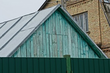 a blue wooden attic under a gray metal roof behind an iron green fence
