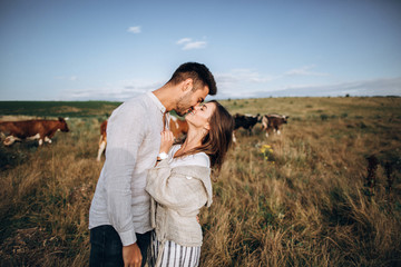 Beautiful loving couple having fun, cuddling, smiling on sky background in field. The guy and the girl hipster kissing