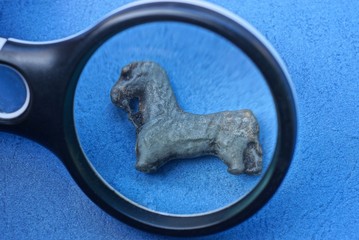 black magnifier magnifies gray old lead toy horse on blue table