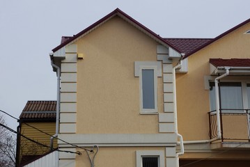 brown attic with one white window on the concrete wall of a private large house against a gray sky on a sunny day