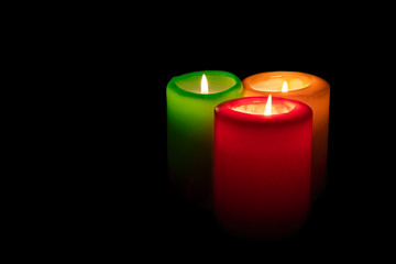 three colored burning candles on a black background closeup