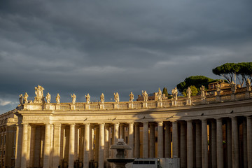 Oświetlona słońcem kolumnada wokół Placu Świętego Piotra w Watykanie na tle burzowych chmur.
