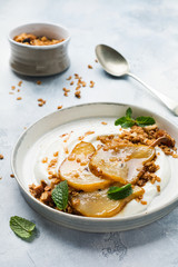 Greek yogurt with caramelized pear, granola, nuts and melted sugar for a wholesome breakfast on a gray ceramic plate. Rustic style. Top view.